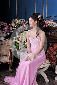 Brunette girl in a pink elegant dress among the flowers in the room