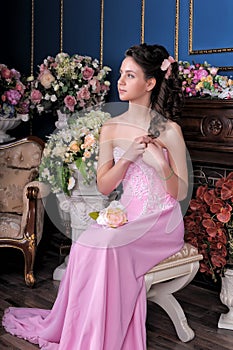 Brunette girl in a pink elegant dress among the flowers in the room
