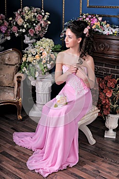 Brunette girl in a pink elegant dress among the flowers in the room