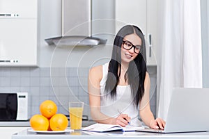 Brunette girl planing day at kitchen and using laptop.