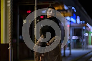 Brunette girl poses against the evening night city, colorful lights illuminate the shopping windows