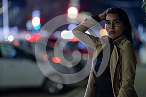 Brunette girl poses against the evening night city, colorful lights illuminate the shopping windows