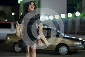 Brunette girl poses against the evening night city, colorful lights illuminate the shopping windows