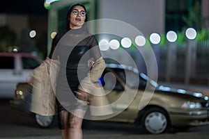 Brunette girl poses against the evening night city, colorful lights illuminate the shopping windows