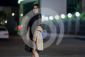 Brunette girl poses against the evening night city, colorful lights illuminate the shopping windows