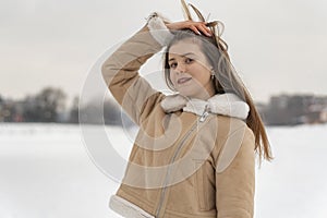 Brunette girl poses beautifully in fashionable beige sheepskin coat decorated with white fur on snowy glade background