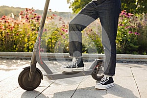 Brunette girl riding an eco-friendly electric kick scooter in a park in sunny weather on sidewalks