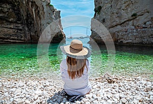 Brunette girl seen from behind sitting on the beautiful beach of Stiniva on the island of Vis in Croatia. Amazing scenery,