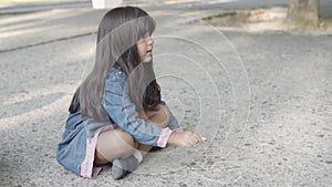 Brunette girl sitting on asphalt and drawing with chalk