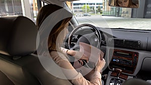 Brunette girl sitting in automobile and searching phone in her purse, back view