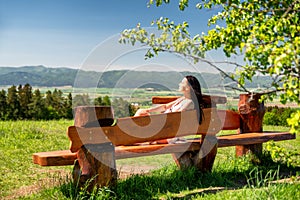 Brunetka sedící na dřevěné lavici v krásné letní zemi