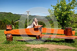 Brunette girl sitting on the wooden bench in beautiful summer country