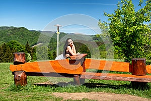 Brunetka sediaca na drevenej lavici v krásnej letnej krajine