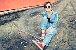 Brunette girl with skateboard sitting, smiling at camera, wearing jeans and modern outfit. Instagram filter, modern concept of