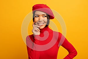Brunette girl smiles with red hat and cardigan. Emotional and joyful expression. Yellow background