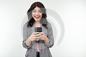 Brunette girl smilingly looks into the smartphone display on a white studio background photo