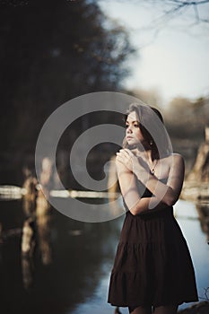 Brunette girl stands by the tree near the water