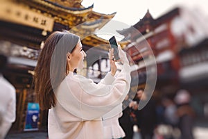 Brunette girl taking photos on her phone of a pagoda in Yuyuan