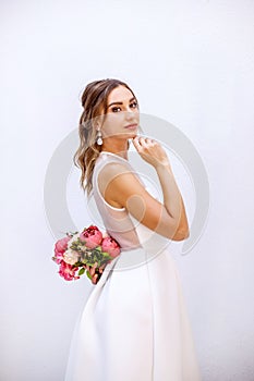 Brunette girl in a wedding dress. Bride in a white dress with a bouquet in her hands. Makeup. photo