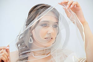 A brunette girl in a wedding dress covers her face with a veil. Bride in a white dress. Makeup. photo