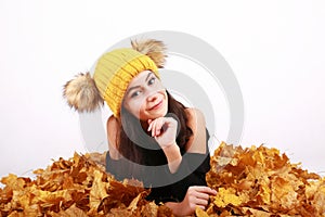 Brunette girl in yellow cap with bobbles lying on autumn leaves