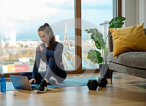 Brunette in green tracksuit browses web on laptop at window photo