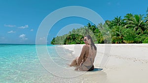 Brunette-haired woman sunbathes on beach against palms