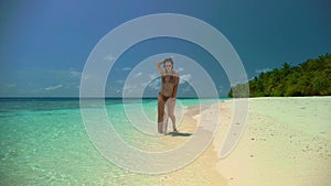 Brunette-haired woman walks along beach edge against palms