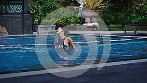 brunette in hot summer day is jumping in swimming pool in Balinese resort splashing with water. Young happy girl