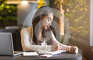 Brunette intelligent girl studying in cafe, making notes