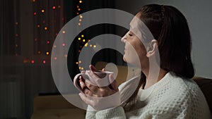 Brunette lady drinks hot coffee sitting on sofa at Christmas