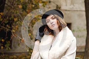 A brunette lady in hat and gloves and coat is standing straightening her hat with her hand. Retro. Outdoors.