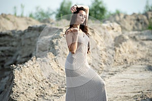 Brunette in light dress stands barefoot on the sand