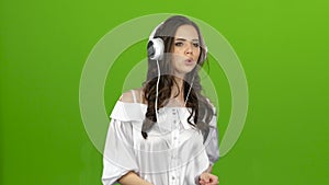 Brunette listens through the headphones with energetic music and builds grimaces. Green screen