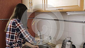 Brunette with long hair in a plaid shirt clears congestion in the sink with the plunger.