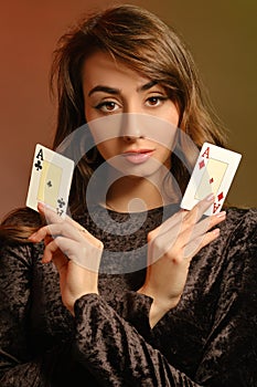 Brunette maiden in black velvet dress and jewelry showing two aces, posing against colorful studio background. Gambling