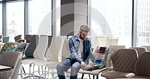 Brunette male with beard sitting, choosing fabric of chairs in modern shopping mall.