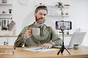 Brunette man recording vlog and holding cup in hand indoor