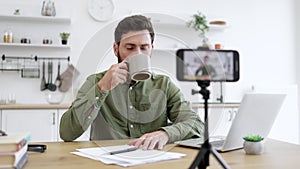 Brunette man recording vlog and holding cup in hand indoor