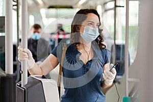 Brunette in medical mask listening to music in city bus