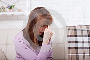 Brunette middle aged woman having headache on home background. Menopause. Copy space