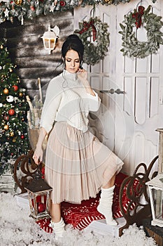 Brunette model girl in tulle skirt and knitted sweater hold lantern, smiles and posing in interior decorated for New