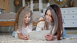 Brunette mom and kid girl play online game on white tablet