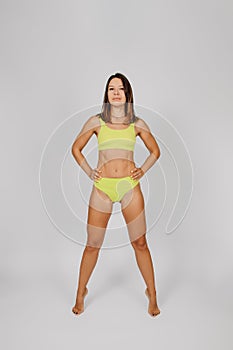 Brunette poses on  background. Young Caucasian woman on light background posing in elegant yellow underwear or