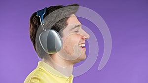 Brunette positive man listening music, enjoying with headphones, violet studio