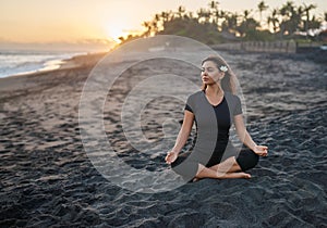 Brunette practicing yoga and meditation in lotus position on the background of the sunset and sea