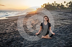 Brunette practicing yoga and meditation in lotus position on the background of the sunset and sea