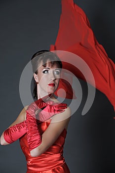 Brunette in a red dress on a gray background in the studio and fluttering fabric