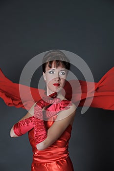 Brunette in a red dress on a gray background in the studio and fluttering fabric