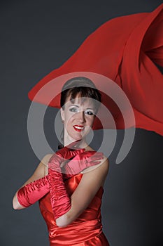 Brunette in a red dress on a gray background in the studio and fluttering fabric